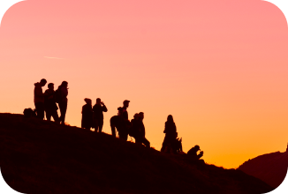 Photo illustratrice de l'approche systémique. Un groupe de personnes se tenant en haut d'une montagne, seulement leurs silhouettes se distinguent par les couleurs du oranger du coucher de soleil.